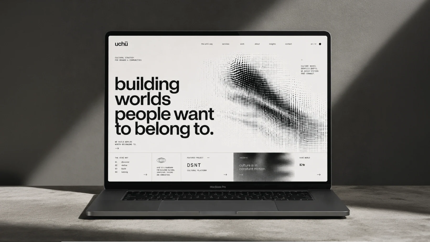De homepage van The Uchu Way op een laptop, hard strijklicht op een betonnen tafel